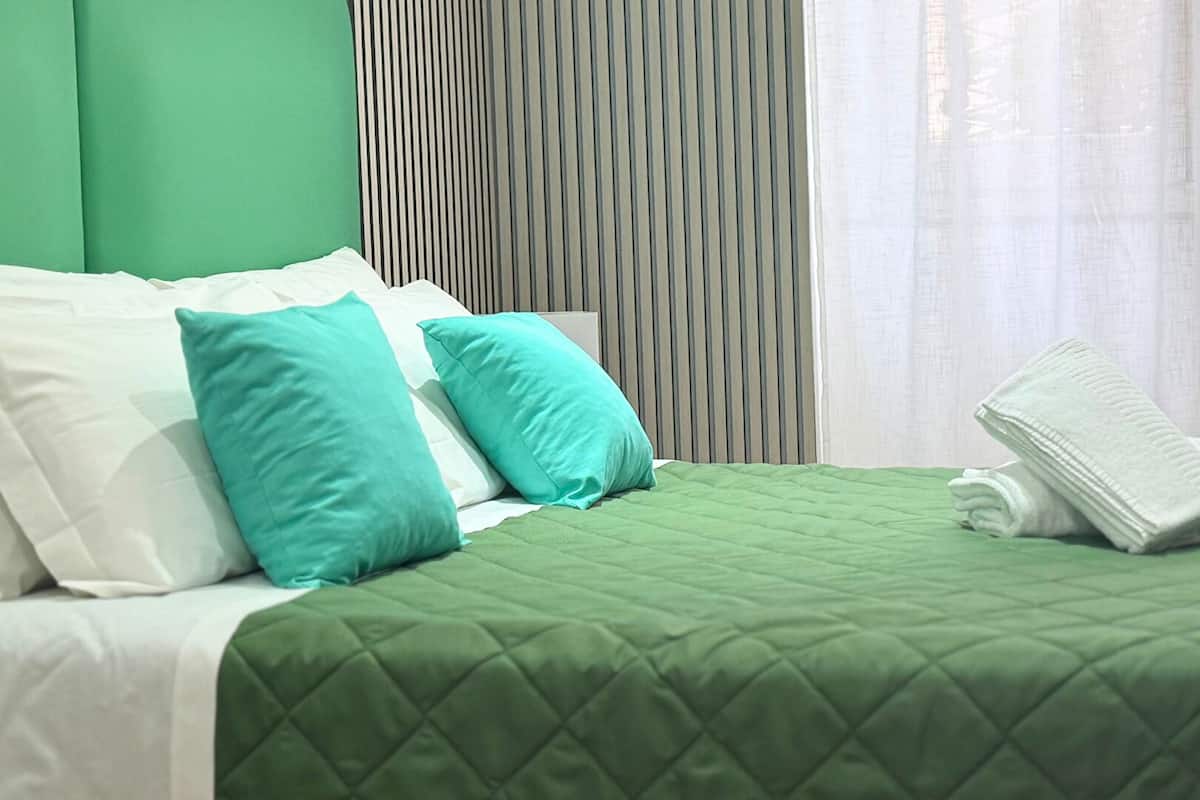 Una cama bien hecha con ropa de cama verde, almohadas blancas y una toalla doblada.