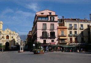 Calle con edificios, incluyendo uno rosa con balcones y un letrero de restaurante.