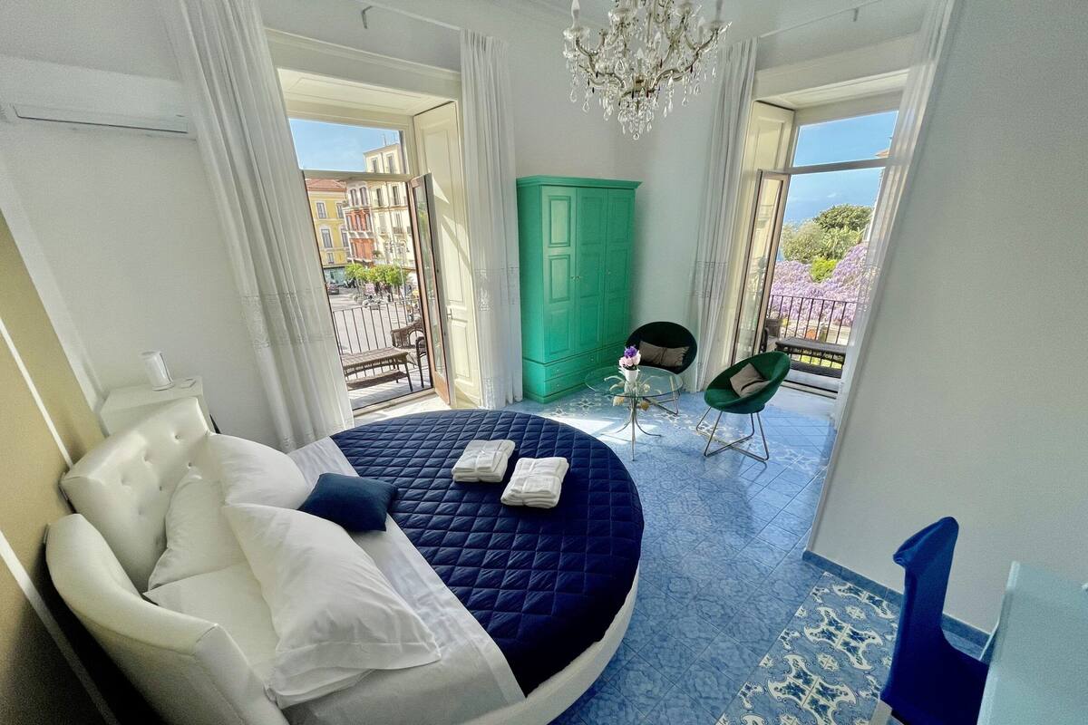 Un dormitorio con cama redonda, armario verde, mesita con un florero y una silla.