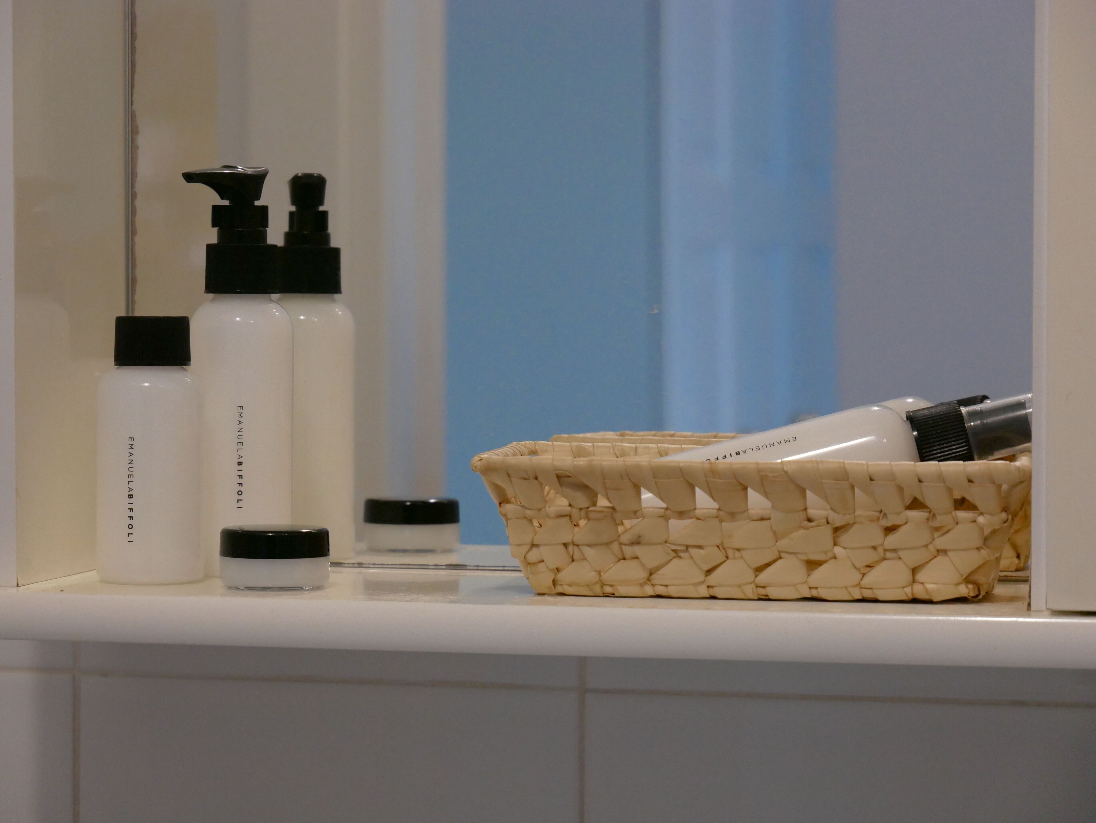 Un meuble-lavabo de salle de bain avec des articles de toilette, notamment des flacons et un panier en osier.