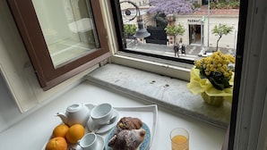 Ein Frühstücksbrett mit Gebäck, Orangen und einem Glas Orangensaft auf einem Fensterbrett.