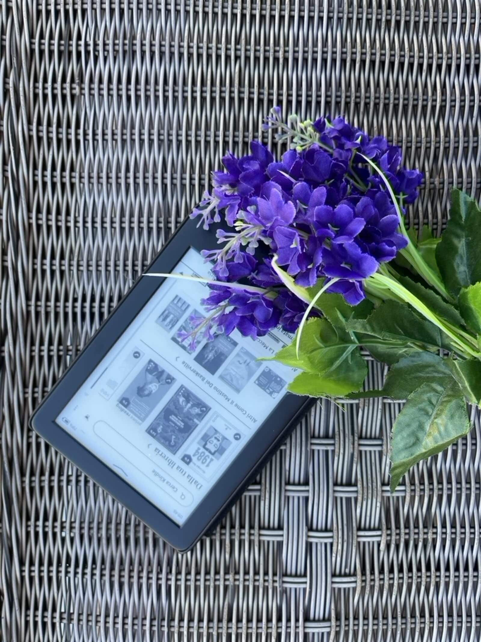 Ein Tablet zeigt eine Zeitschrift oder ein Buch auf einer Korboberfläche, dazu ein Strauß lila Blumen.