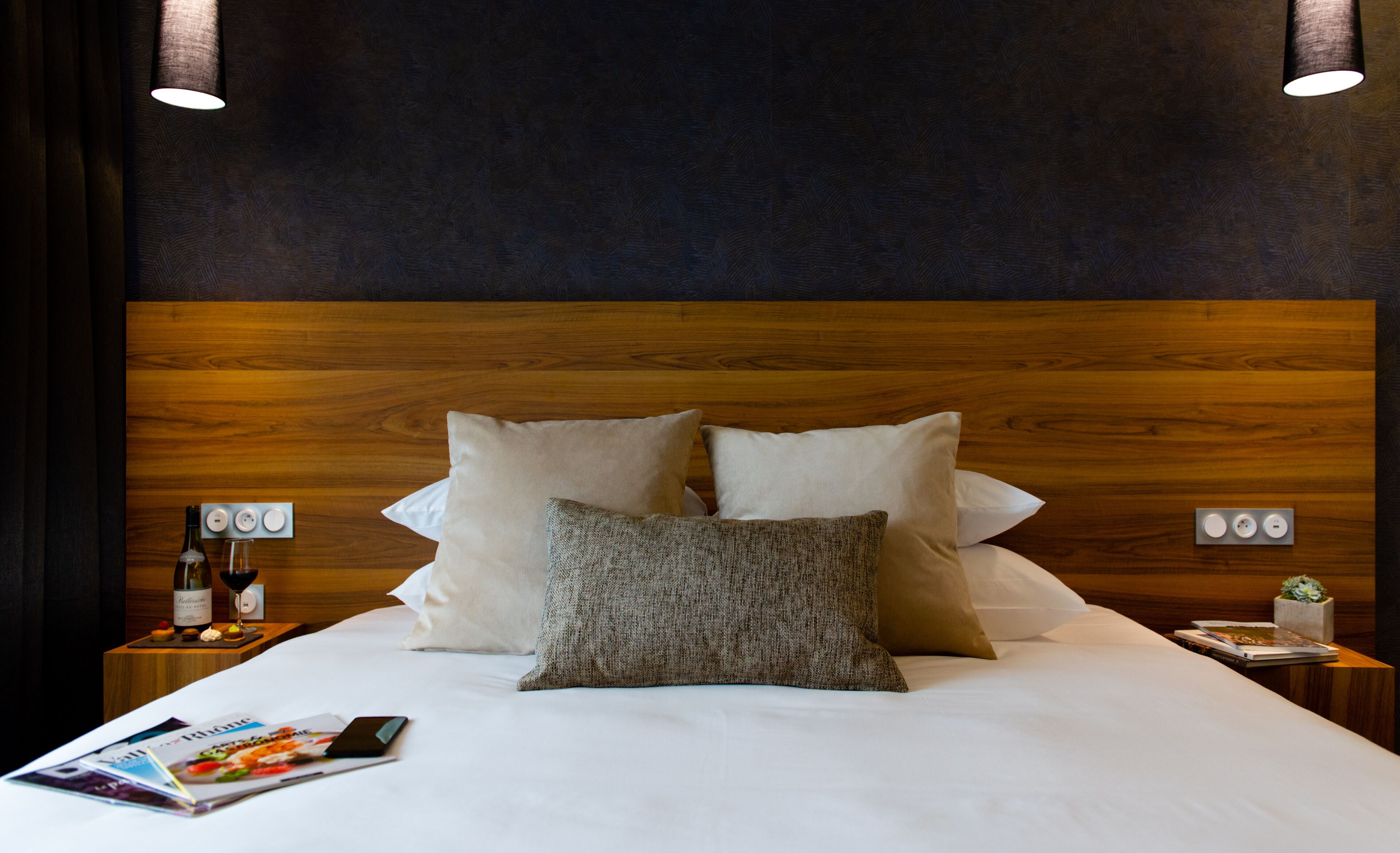A neatly made bed with a wooden headboard, two bedside tables with lamps, and a magazine on the bed.