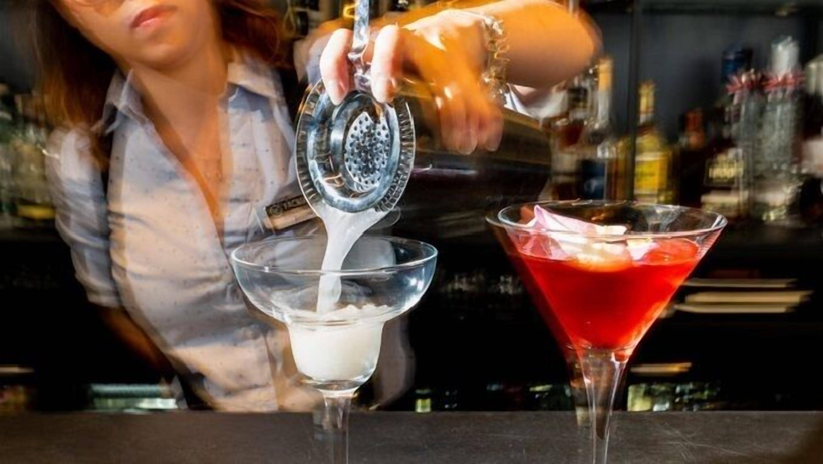 Un cantinero preparando un cóctel con un agitador y una copa de martini.