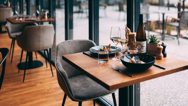 Une scène de restaurant avec une table dressée pour deux personnes, comprenant un plat, des verres à vin et une bouteille de vin.