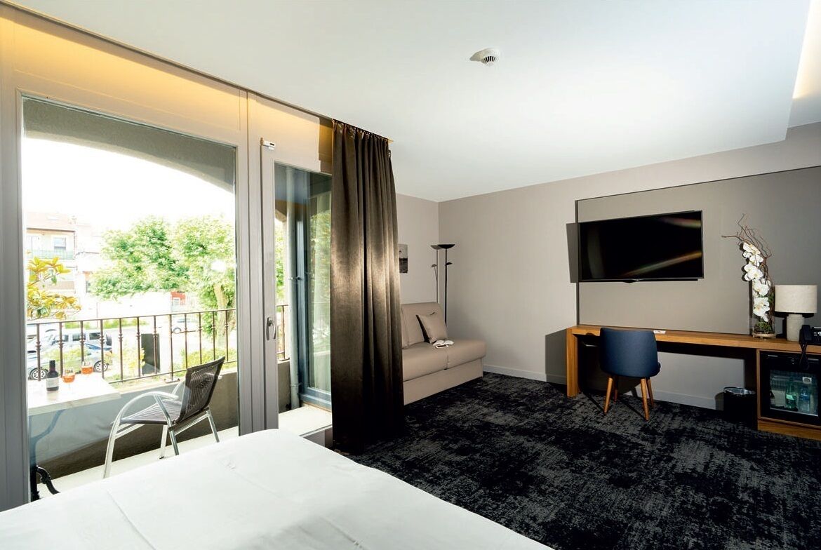 A hotel room with a bed, a desk, a chair, a TV, and a balcony with a view of the outside.