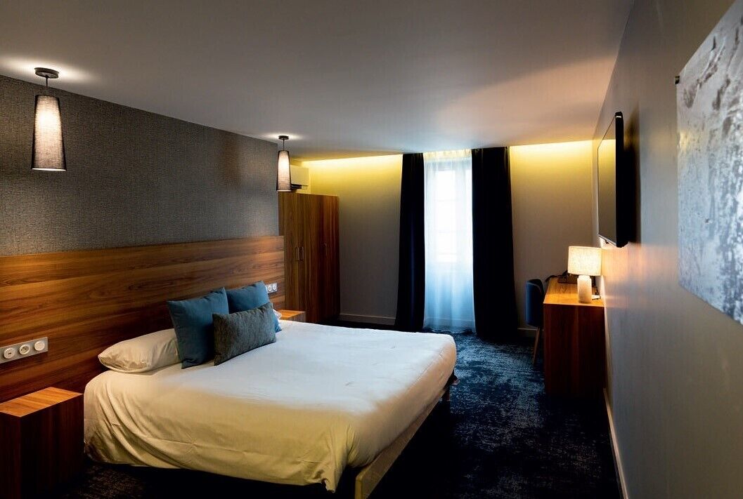 A hotel room with a large bed, a wooden headboard, a nightstand with a lamp, and a wall-mounted TV.