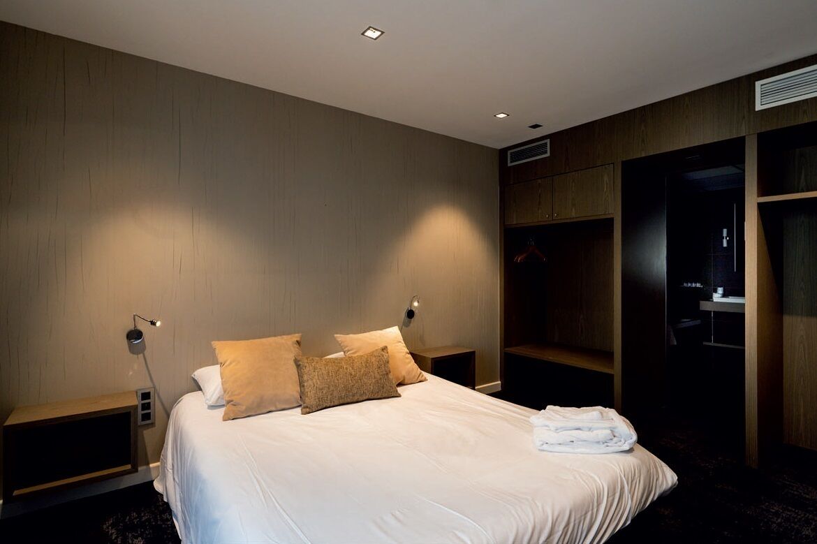 A hotel room with a large bed, two bedside tables, a wardrobe, and a mirror.