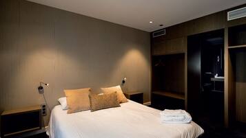 A hotel room with a large bed, two bedside tables, a wardrobe, and a mirror.