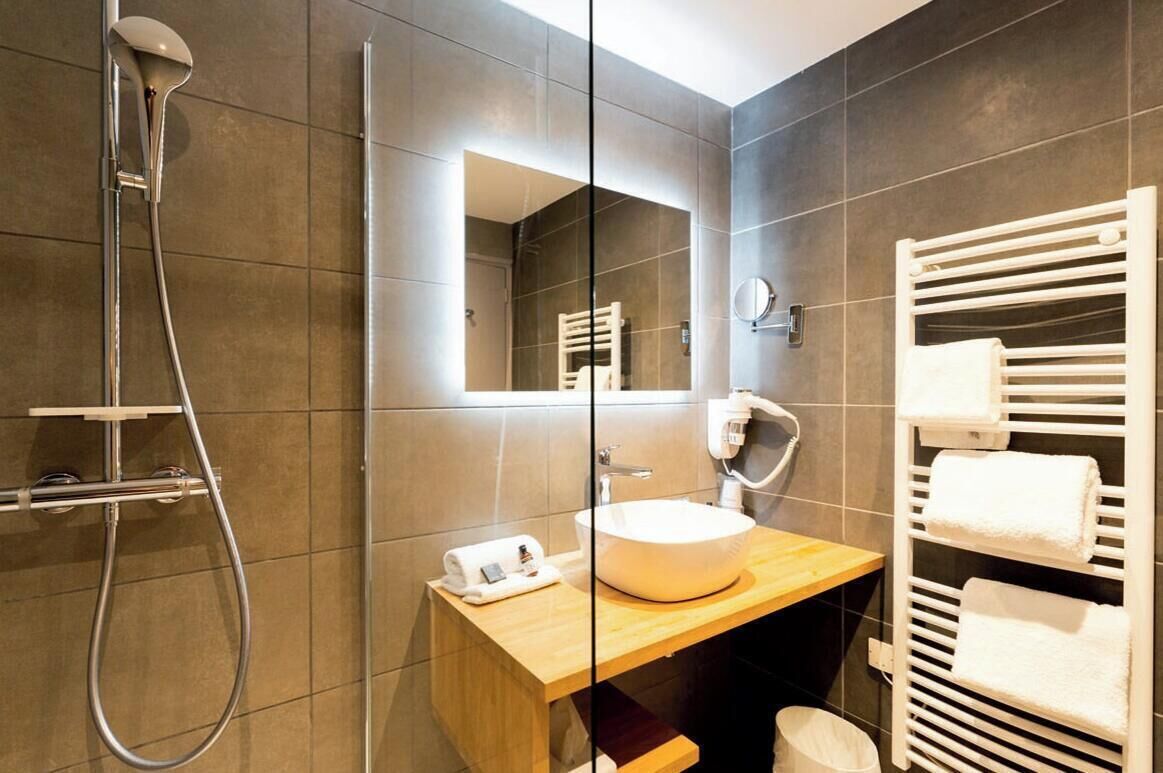 A modern bathroom with a glass shower enclosure, a wooden vanity, a large mirror, and a towel rack.