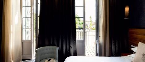A hotel room with a bed, a chair, and a view of the outside balcony.