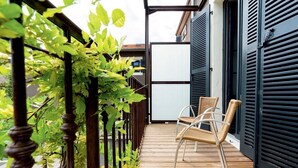 Une terrasse en bois avec deux chaises en osier, une rambarde en métal et un bâtiment aux volets sombres.