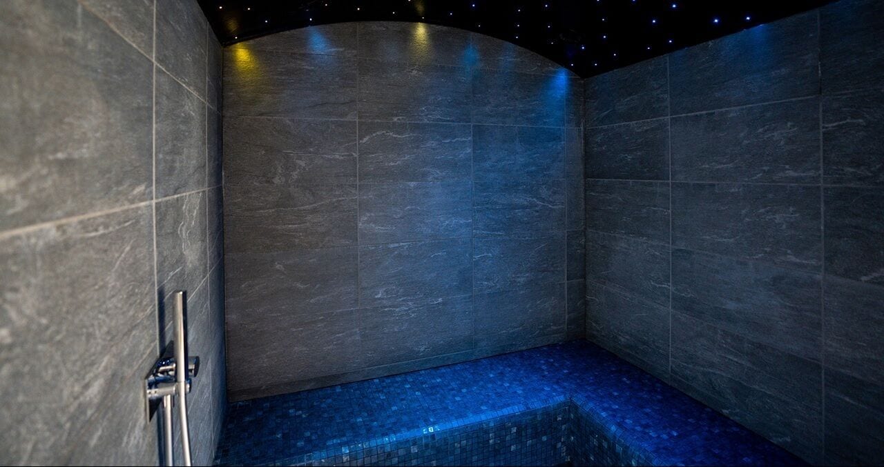 A modern bathroom with dark marble walls and a blue-tiled floor.