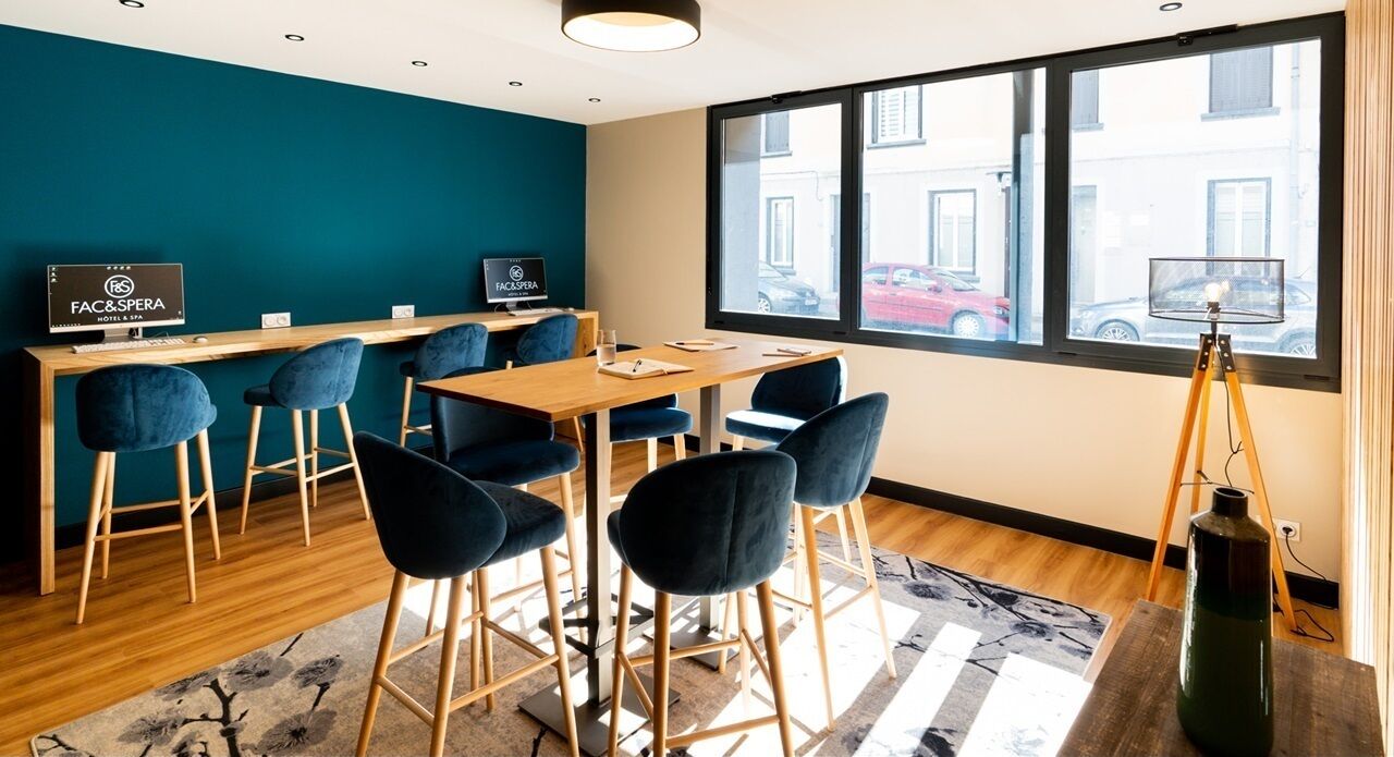 Uma sala de reunião moderna com uma mesa de madeira, cadeiras azuis e uma janela ampla com vista para a rua.