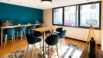 Uma sala de reunião moderna com uma mesa de madeira, cadeiras azuis e uma janela ampla com vista para a rua.