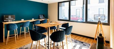Una sala de reuniones moderna con una mesa de madera, sillas azules y un ventanal con vista a la calle.