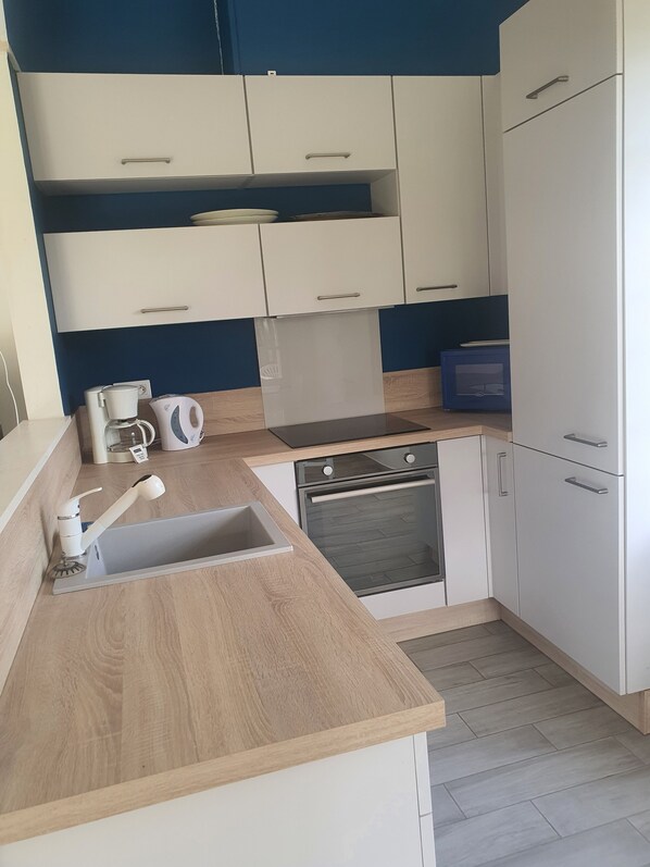 A modern kitchen with white cabinets, a wooden countertop, a built-in oven, and a sink. - Cottage/gîte à Labri de Lagitation Dans un Environnement Calme et Serein (Decize)