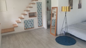 Un dormitorio con una cama, una alfombra azul, una lámpara de pie, un espejo y una escalera con escalones de madera y paneles azules estampados.