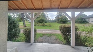 Un espacio al aire libre techado con vista a un césped, árboles y un edificio en la distancia.