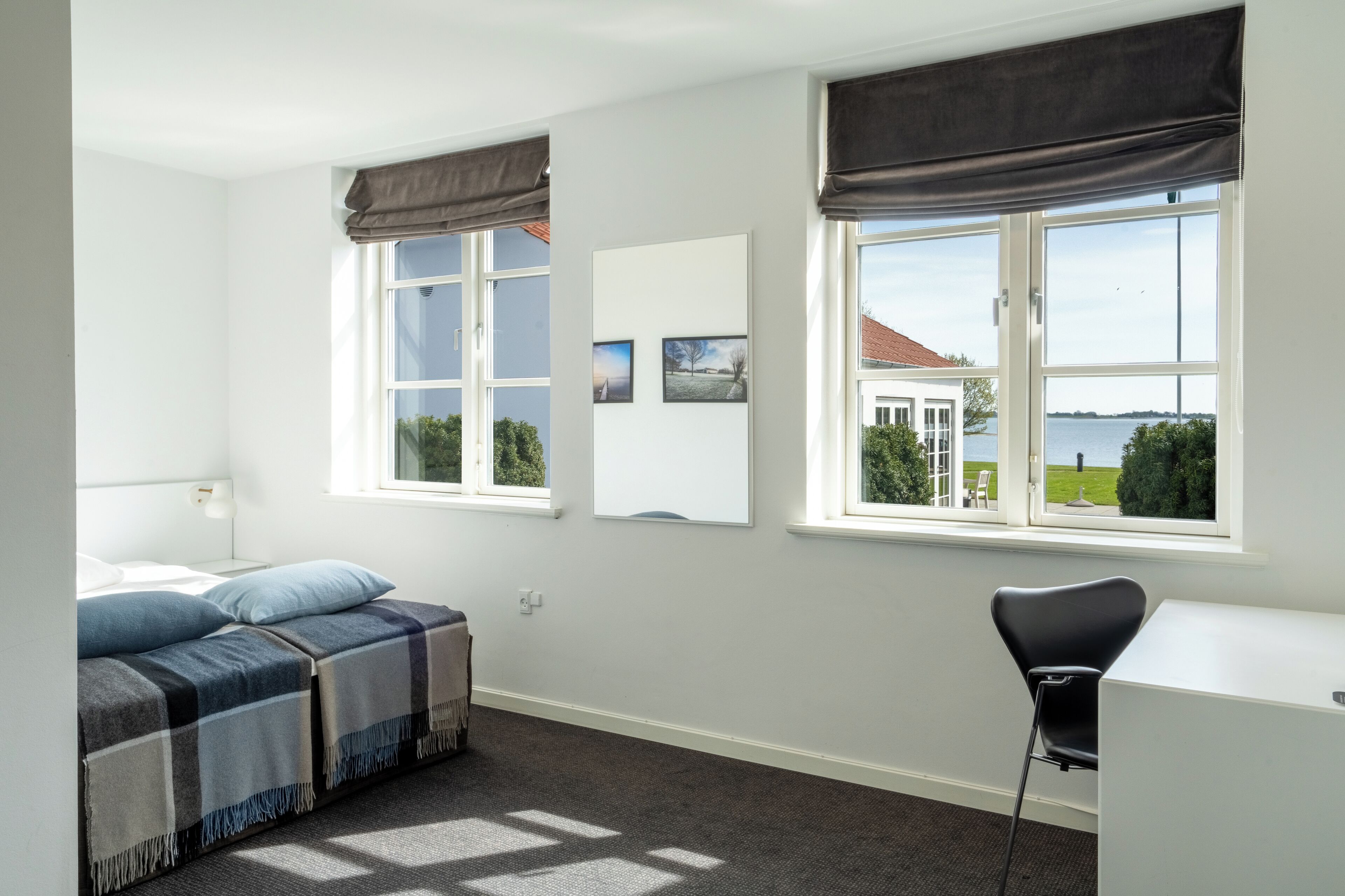 Un dormitorio con cama, escritorio y vista a una casa y al agua.