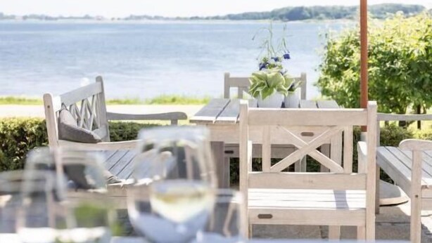 An outdoor dining area with a table set for two, a white umbrella, and a view of the water. - Borre Knob Fjordhotel (Horsens)