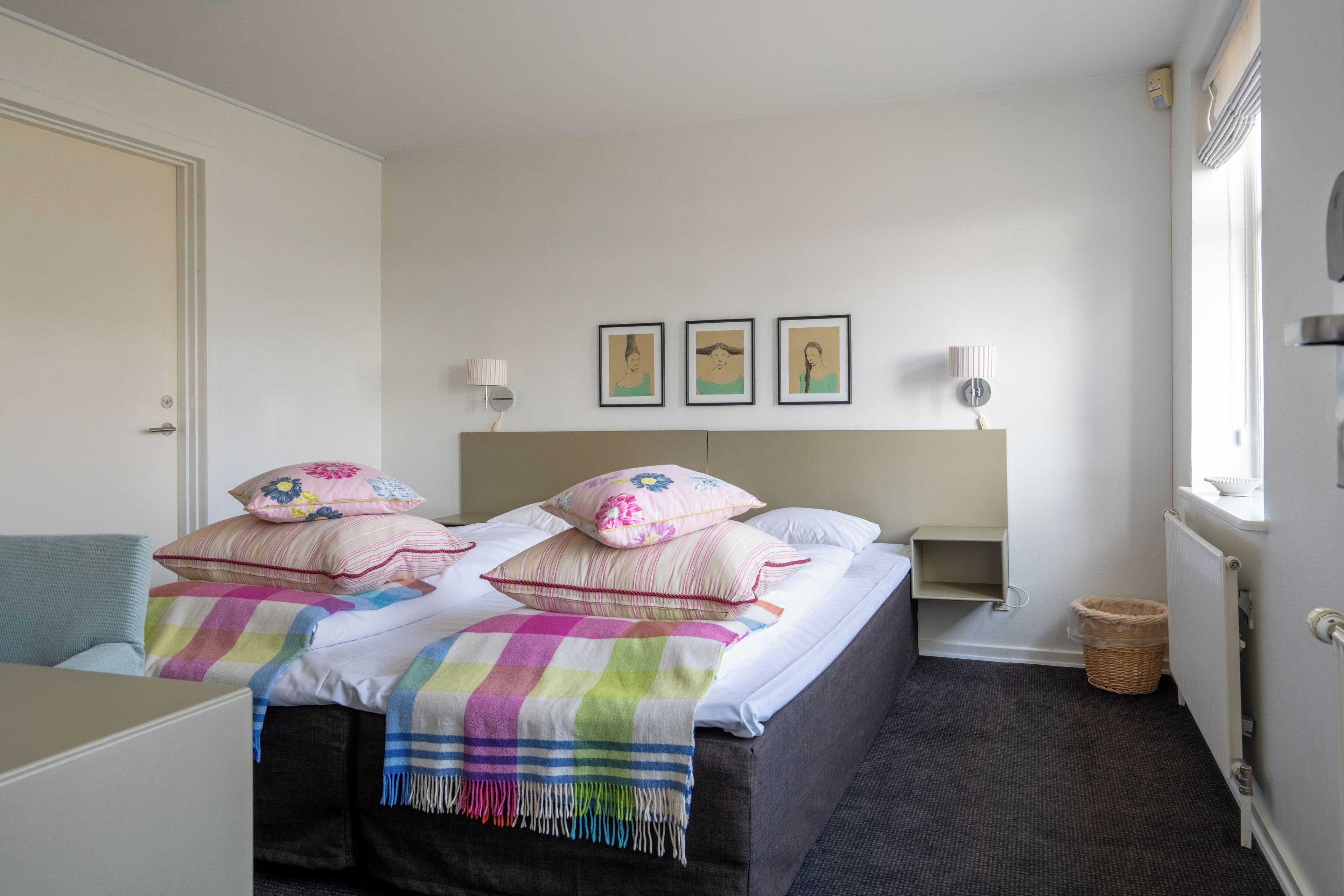 A hotel room with a bed, two bedside tables, a lamp, a wall-mounted shelf, and a window.