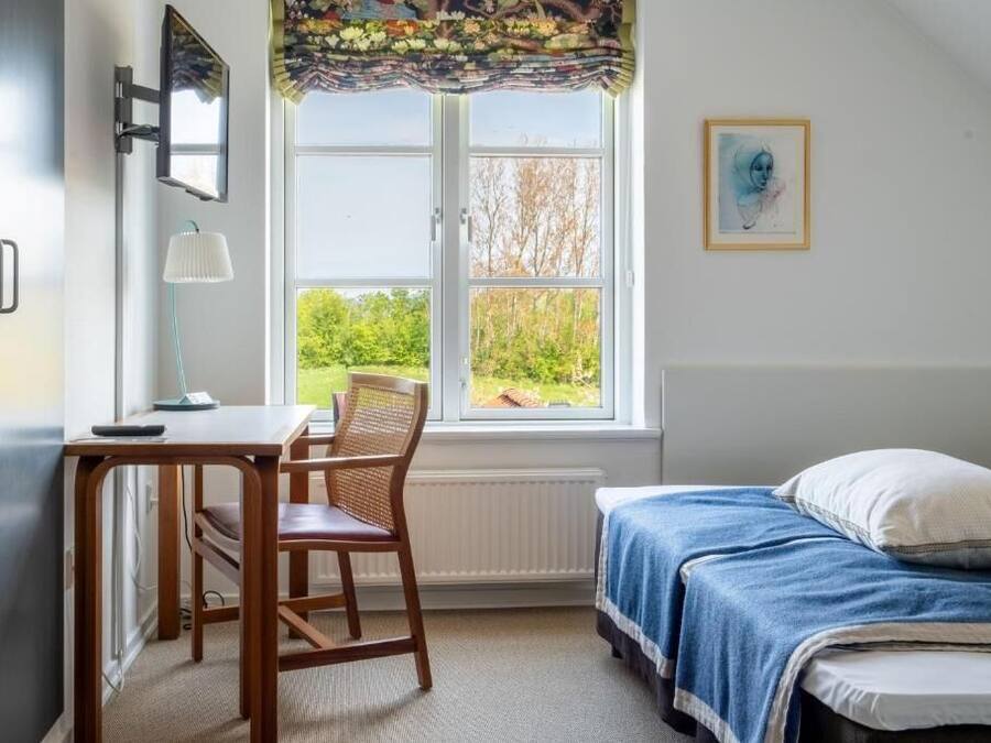 Quarto com cama, escrivaninha, cadeira, janela com vista para o verde e quadro na parede.