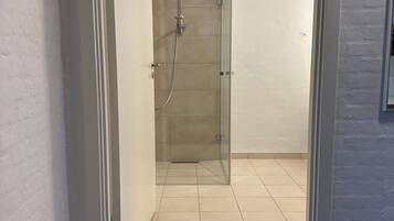 Een moderne badkamer met een douchecabine van glas, een vloer met witte tegels en een zwarte, geribbelde mat bij de ingang.