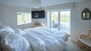 A bedroom with a large bed, a television mounted on the wall, a window with a view of the outdoors, and a wicker chair. - Borre Knob Fjordhotel (Horsens)