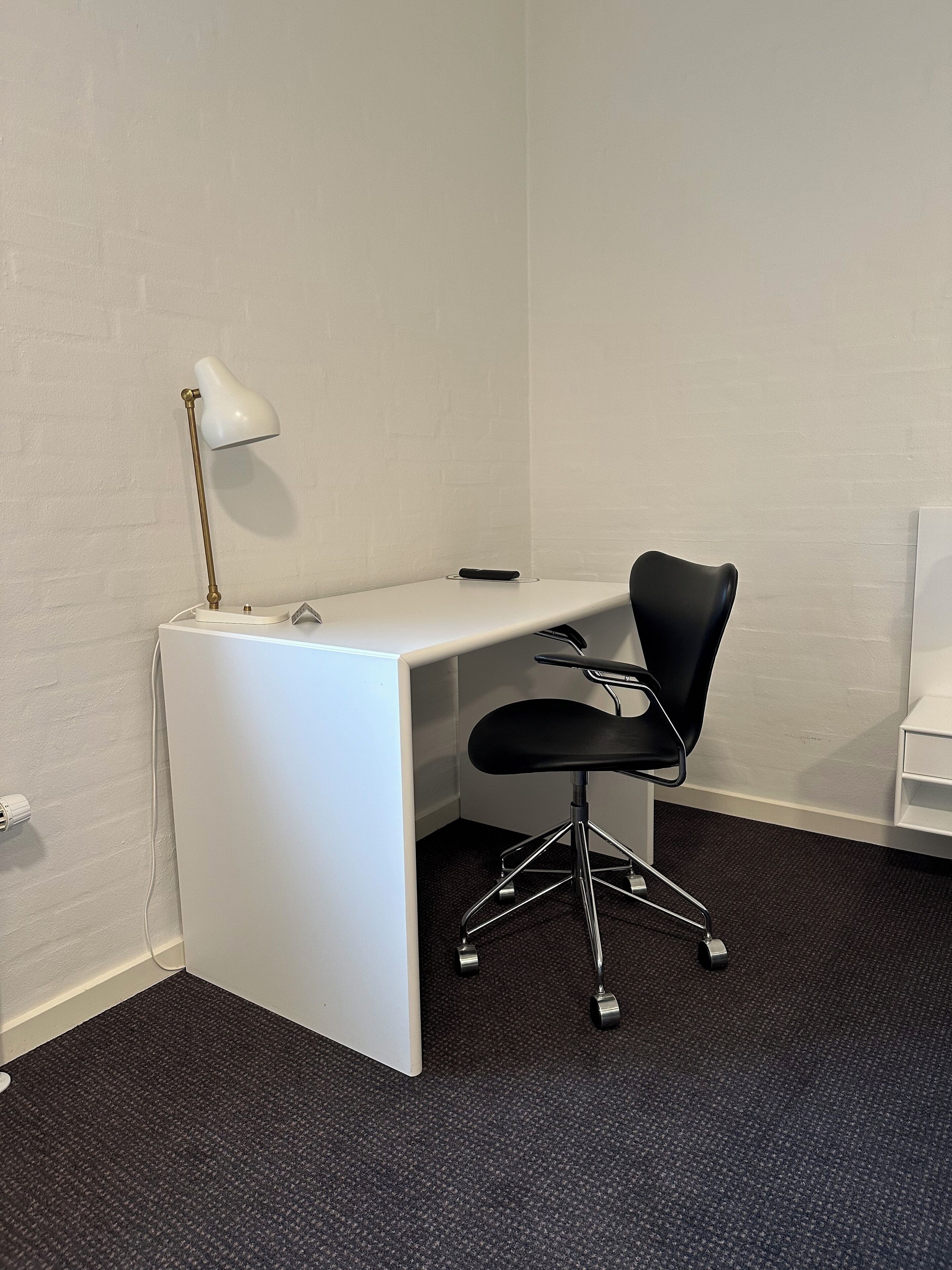A small office space with a white desk, a black office chair, and a white lamp.