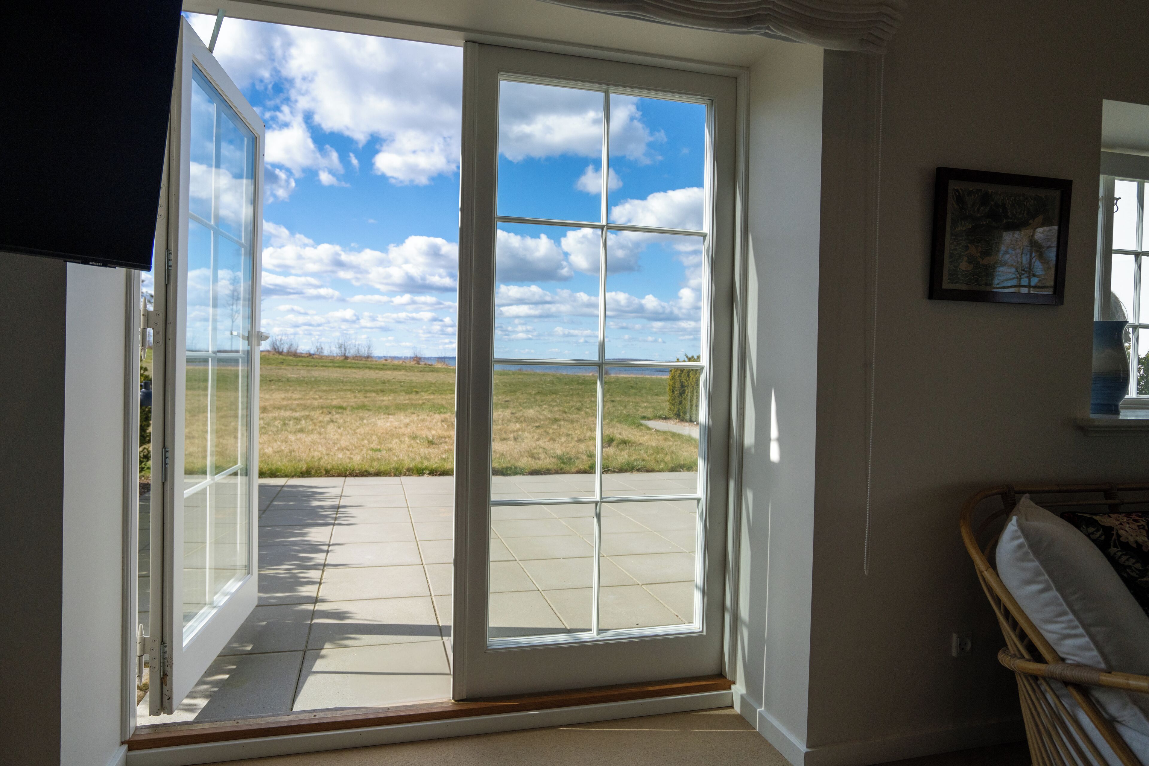 A room with a large sliding glass door leading to a patio with a view of a grassy field and a body of water.