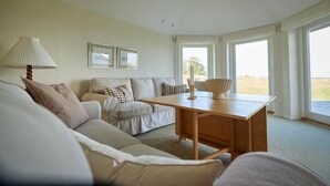 A living room with a sofa, a wooden table, and a lamp. There are two windows with curtains. - Borre Knob Fjordhotel (Horsens)