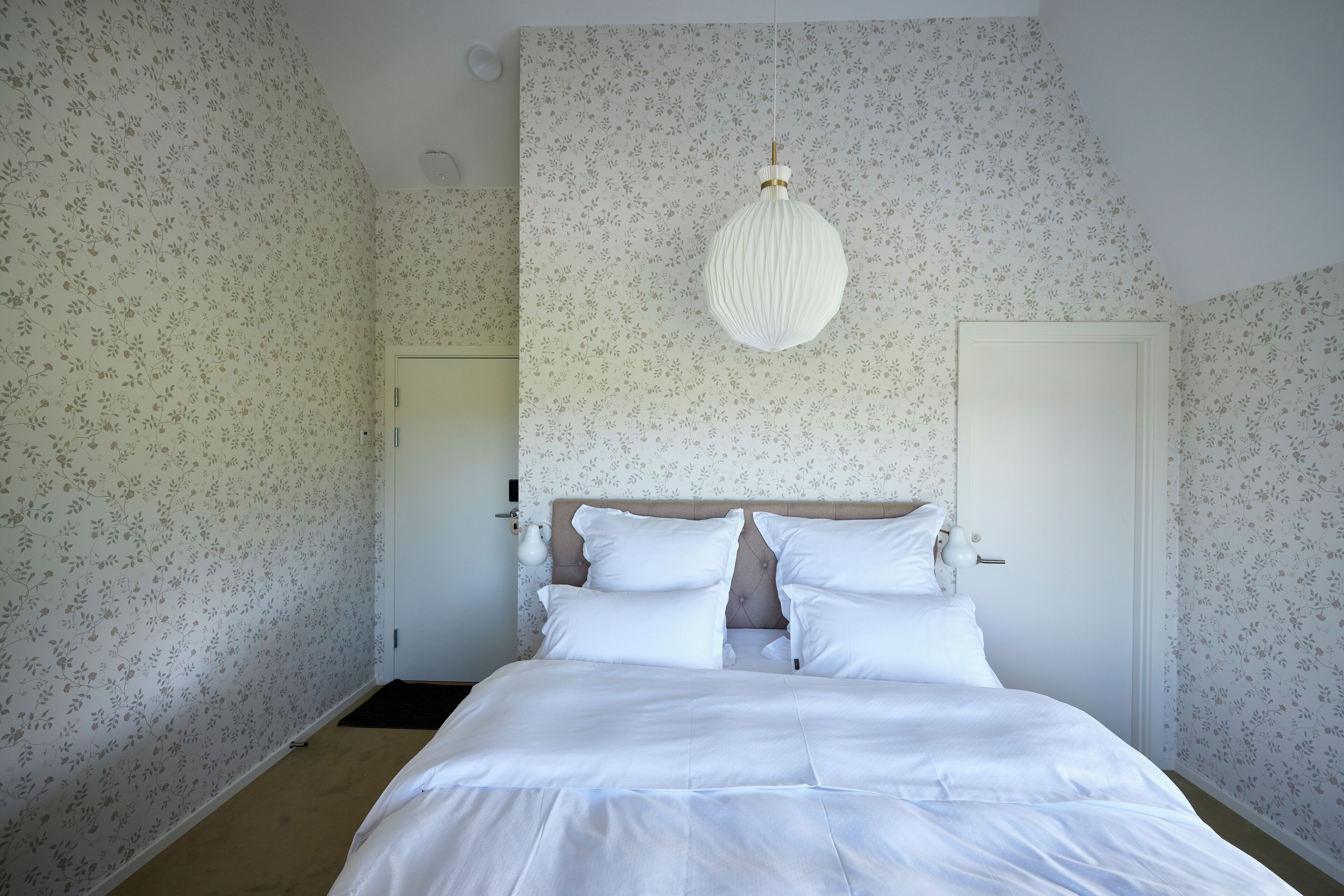 Un dormitorio con cama, papel tapiz floral, lámpara colgante y una puerta.