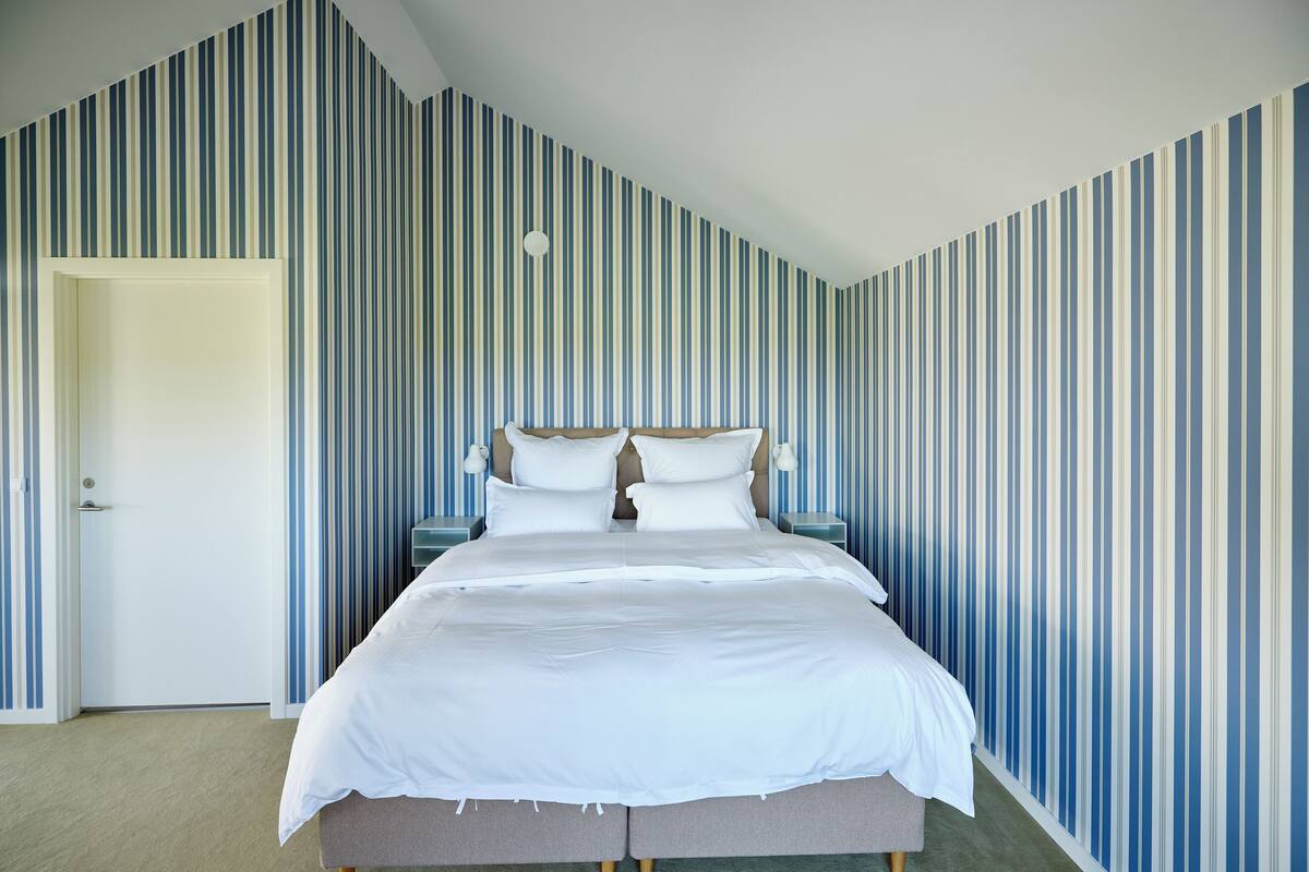 Un dormitorio con una cama grande, papel tapiz a rayas, una puerta y mesitas de noche.