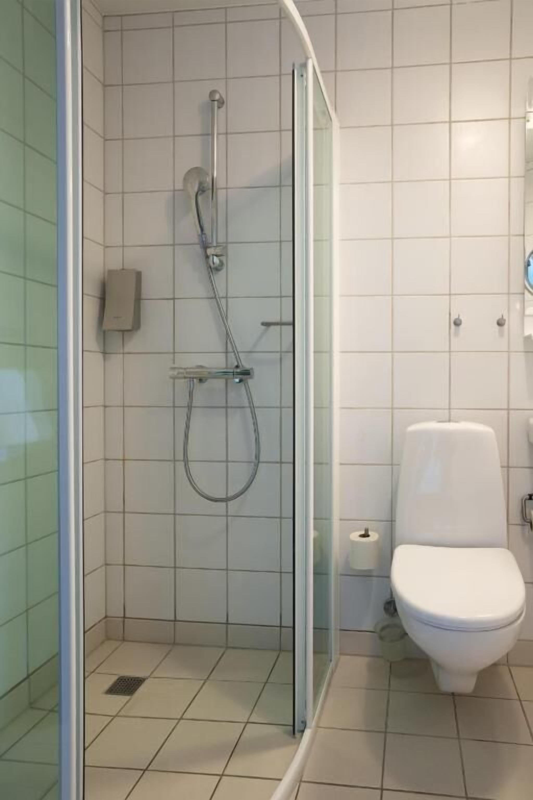 Une salle de bain moderne avec une douche à parois de verre, des toilettes et une petite poubelle.