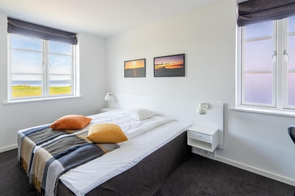 Een hotelkamer met een bed, twee nachtkastjes, een raam met uitzicht op zee en twee ingelijste foto's aan de muur.