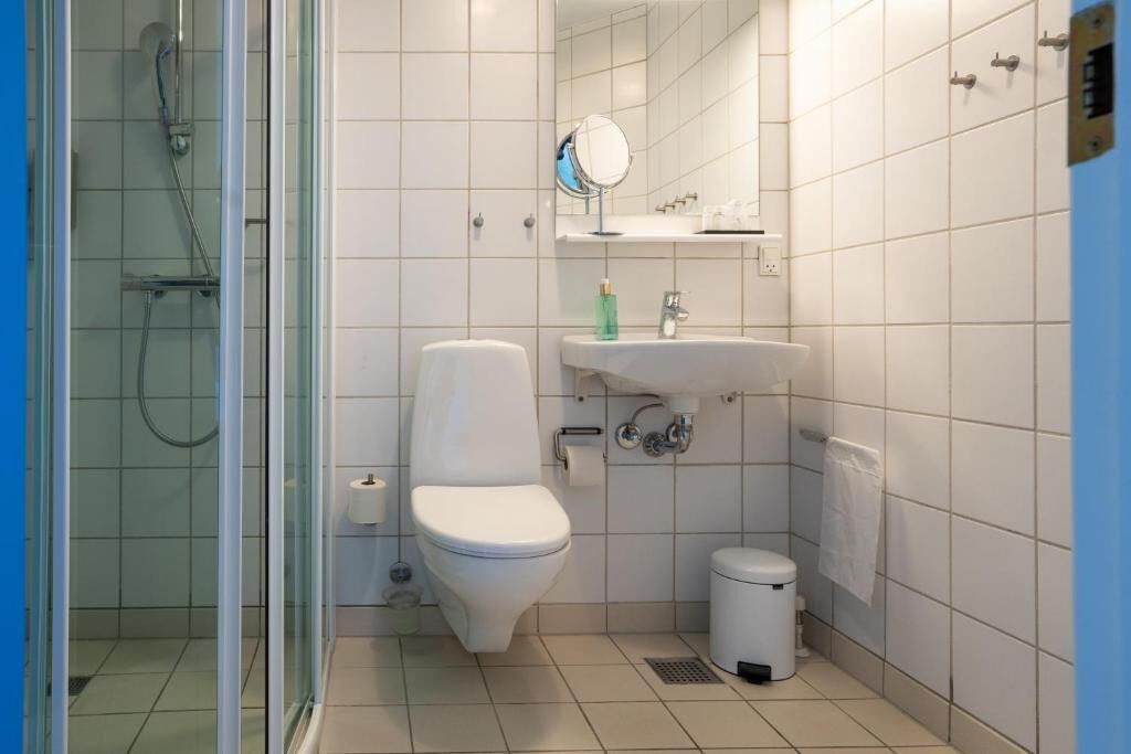 Un baño moderno con ducha de vidrio, inodoro blanco, lavamanos con espejo y un cubo de basura.