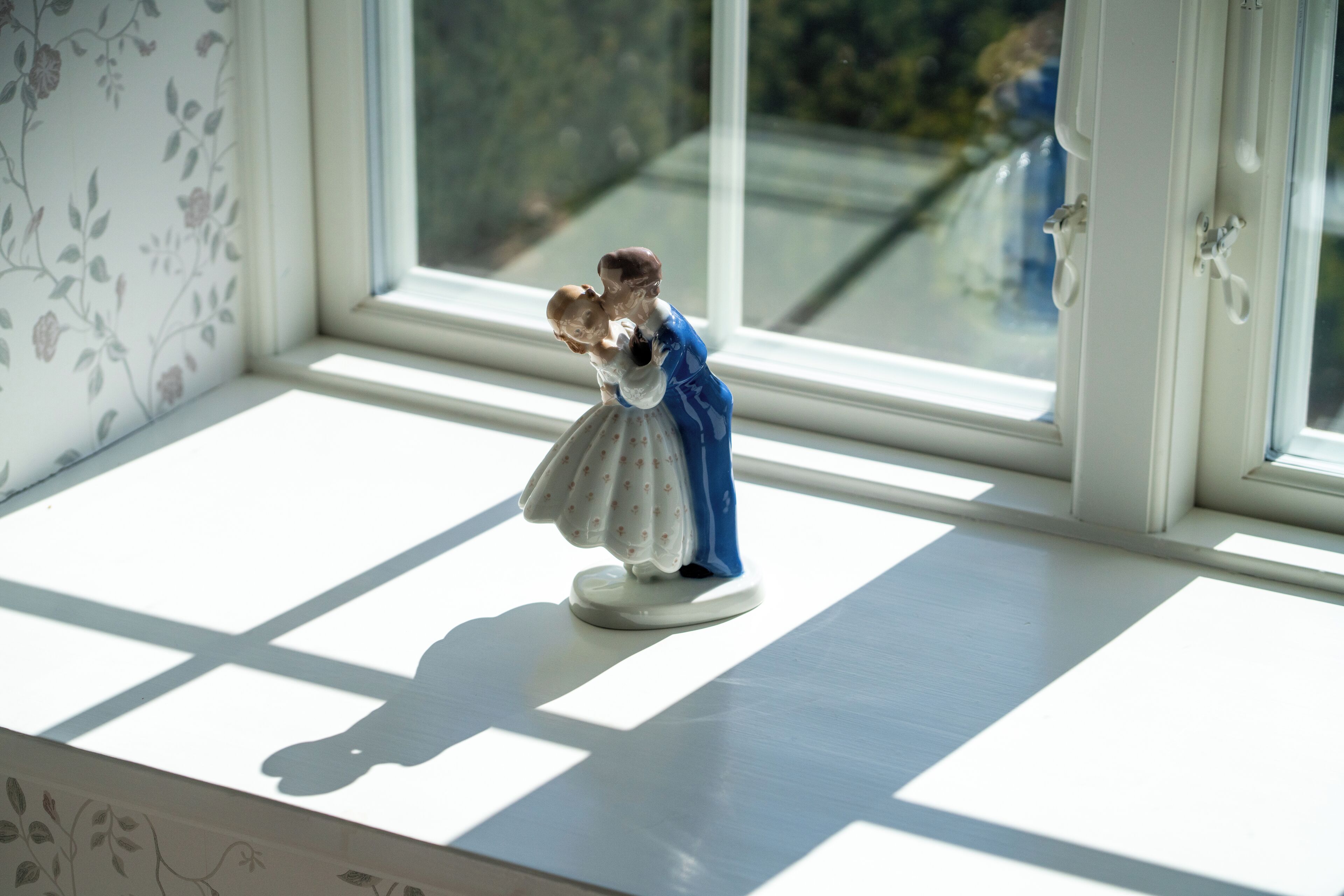A figurine on a windowsill with a view of greenery outside.