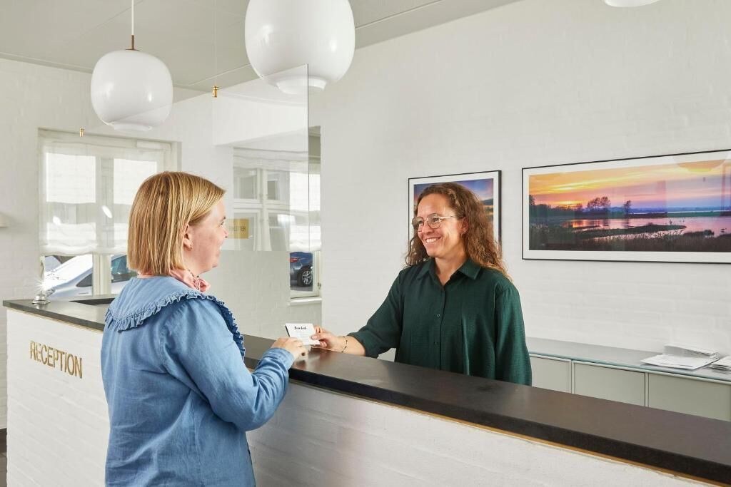Un espace d’accueil comprenant un comptoir de réception, une enseigne indiquant « RÉCEPTION » et deux tableaux encadrés accrochés au mur.