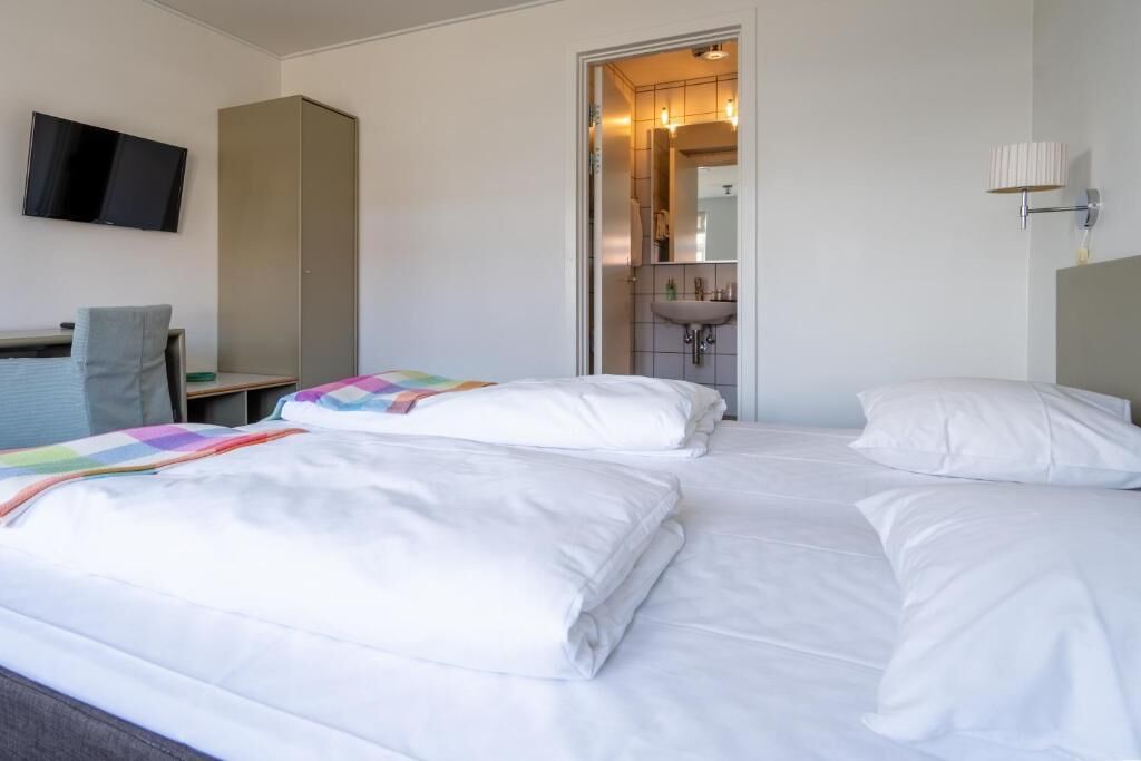 Habitación de hotel con dos camas, un escritorio, una silla, un televisor y un baño visible a través de una puerta abierta.