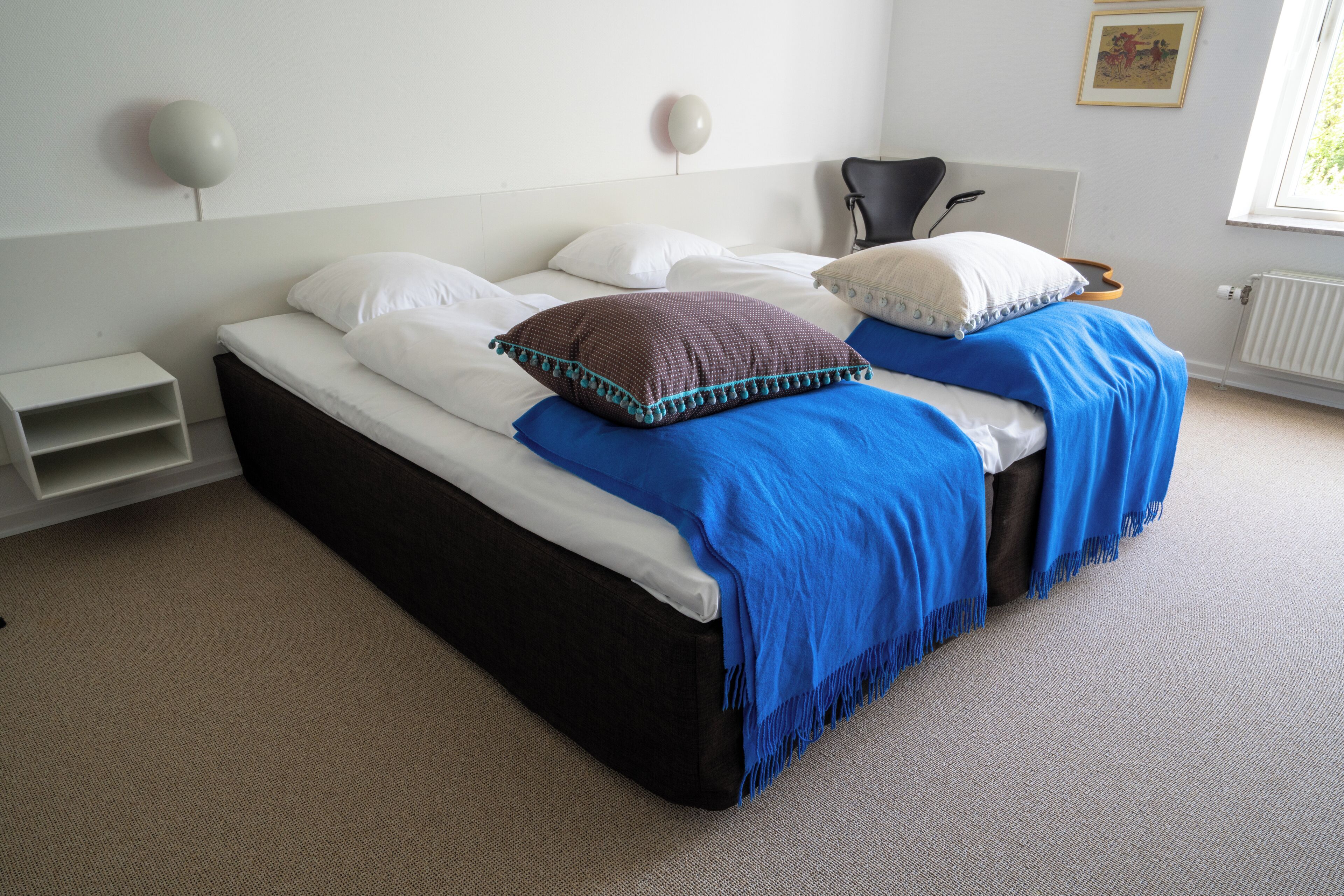 Una cama con ropa de cama blanca y azul, una mesita de noche pequeña y una silla.