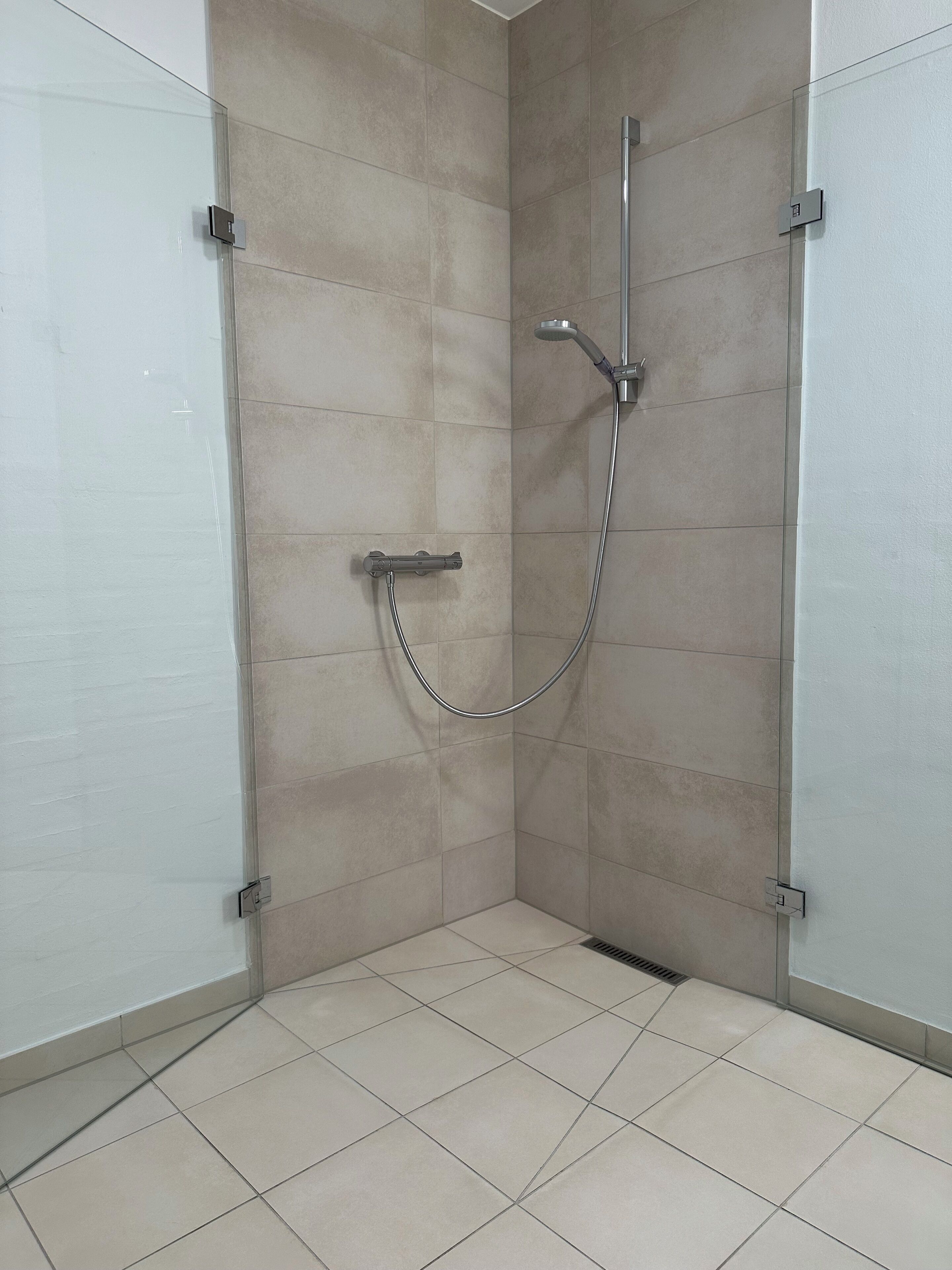 A shower area with a glass door, tiled walls, and a tiled floor.
