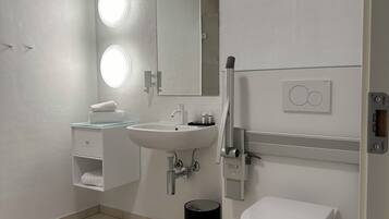 Un baño moderno con lavamanos blanco, espejo y retrete. Hay dos luces iluminadas sobre el espejo y un cubo de basura negro junto al retrete.