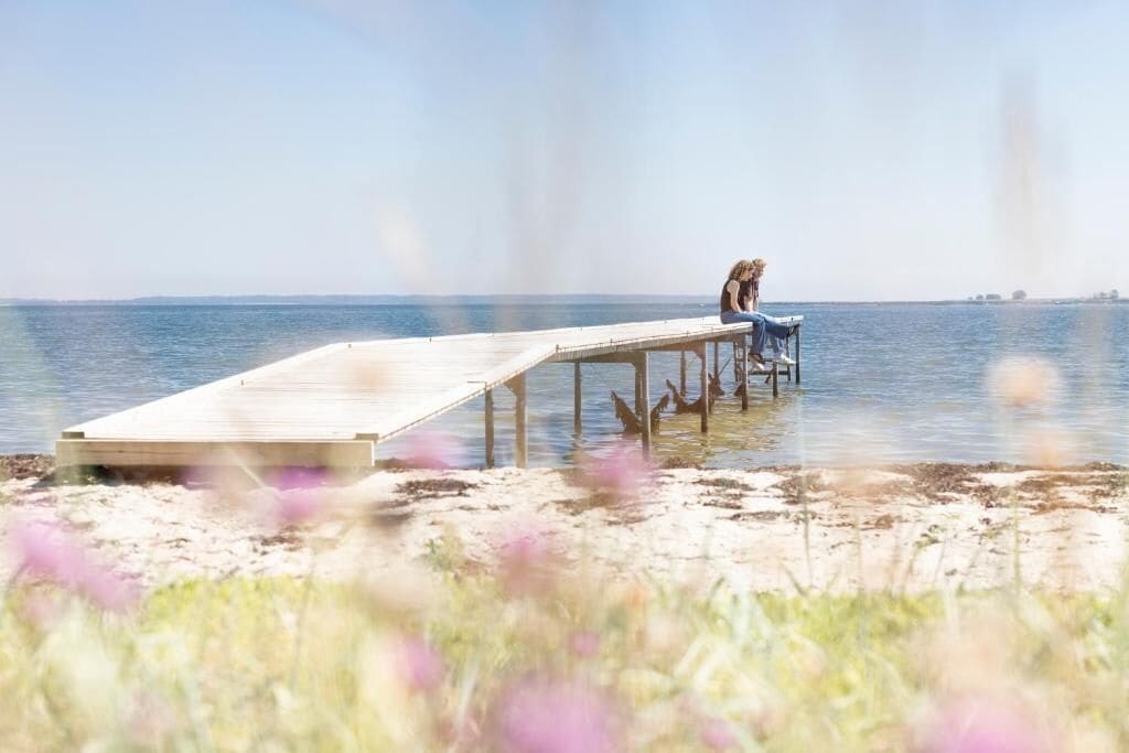 Une jetée en bois s’étendant dans des eaux calmes, avec une personne assise à son extrémité.