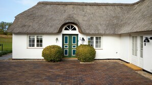 A white building with a thatched roof, a green door, and a brick pathway leading to the entrance. - Borre Knob Fjordhotel (Horsens)