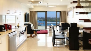 A modern kitchen with a dishwasher, stove, and a dining area with a table and chairs. - Penthouse Pads (Darwin)