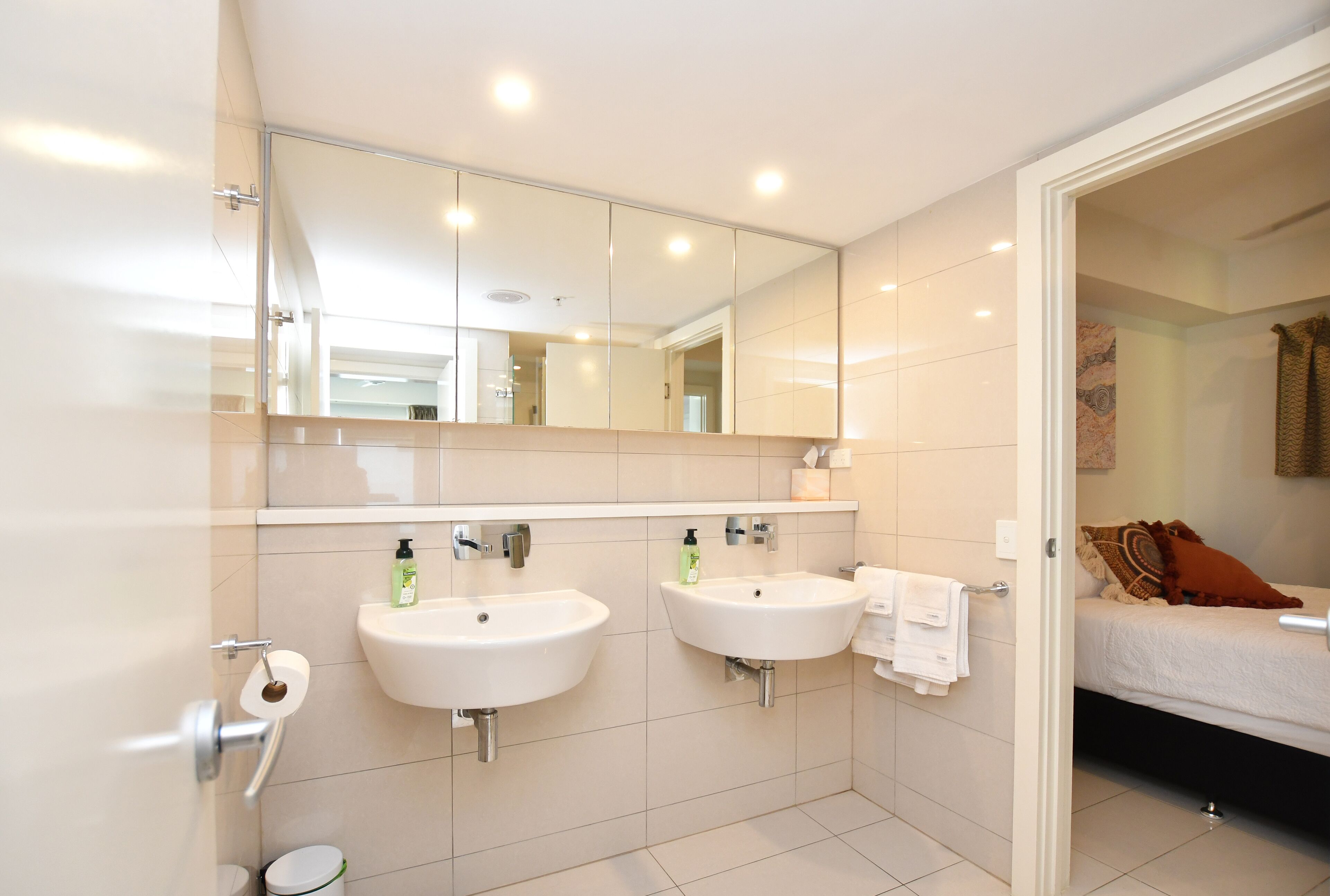 A modern bathroom with two sinks, a toilet, and a mirror.