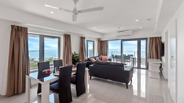 A modern living room with a dining area, large windows, and a view of the sea. - Penthouse Pads (Darwin)