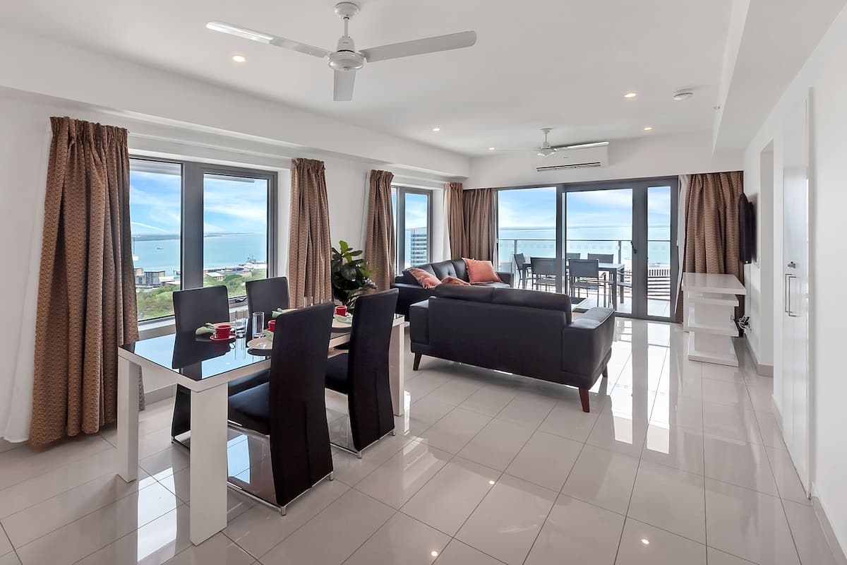 A modern living room with a dining area, large windows, and a view of the sea.