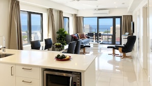 A modern kitchen with a built-in microwave, a dining area with a table and chairs, and a large window offering a view of the sea. - Penthouse Pads (Darwin)